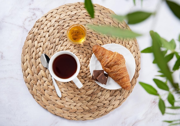 Concepto de desayuno con una taza de miel de té y un croissant en una mesa de mármol y ramas verdes en primer plano Vista superior