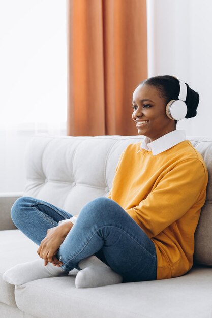 Concepto de descanso y relajación. Tranquila mujer negra sentada en una bolsa de frijoles, escuchando música, audiolibros, podcasts, disfrutando de la meditación para dormir y la mente en paz con auriculares inalámbricos, reclinándose, copiando espacio