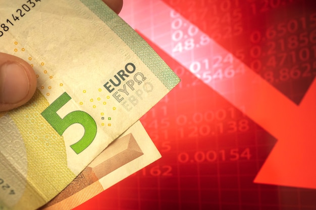 Concepto descendente de dinero en euros, billetes en euros en la mano, moneda bajando fondo de flecha roja, finanzas y fotografía de negocios