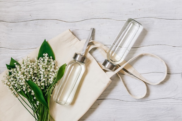 Concepto de desperdicio cero. Botellas de agua de vidrio y bolsa ecológica sobre una mesa de madera blanca.