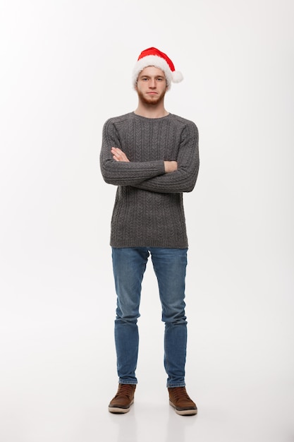 Concepto del día de fiesta - El hombre joven de la barba en suéter cruzó los brazos que presentaban en el fondo blanco.