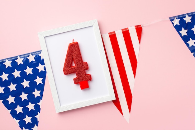 Concepto del Día de la Independencia de EE. UU. Foto de vista superior del marco de fotos con vela número 4 sobre guirnalda de bandera nacional sobre fondo rosa pastel aislado