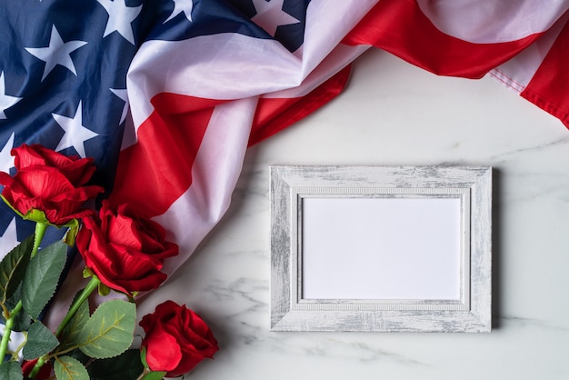 Concepto de día de la independencia de Estados Unidos o día de los caídos. Bandera nacional y rosa roja sobre fondo de mesa de mármol brillante con marco de imagen.