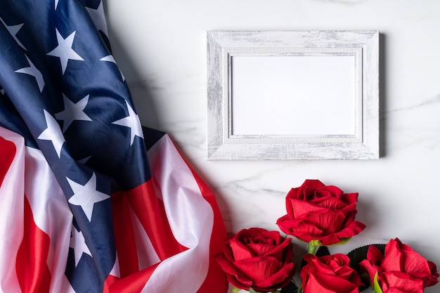 Concepto de día de la independencia de Estados Unidos o día de los caídos. Bandera nacional y rosa roja sobre fondo de mesa de mármol brillante con marco de imagen.