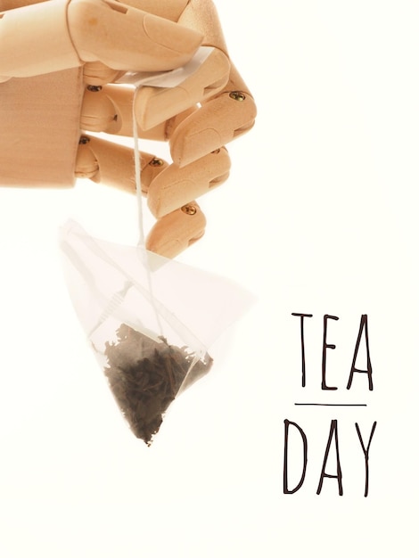 Foto concepto del día internacional del té mano de madera sosteniendo una bolsa de té y texto sobre un fondo blanco