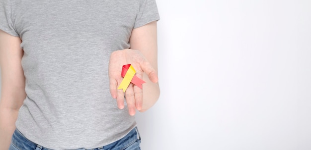 Concepto del Día Mundial contra la Hepatitis. Chica en camiseta gris tiene en su mano cinta roja-amarilla símbolo de conciencia. Fondo gris. Copia espacio