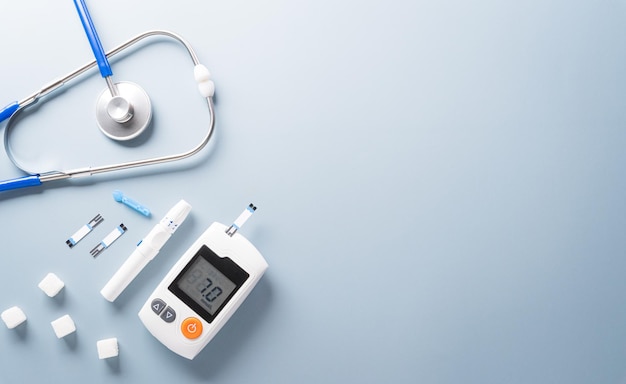 Concepto del día mundial de la diabetes 14 de noviembre Vista superior de los juegos de medidores de glucosa en sangre y estetoscopio sobre fondo azul pastel