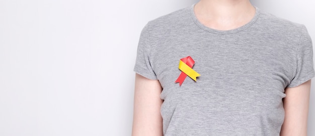 Concepto del día mundial de la hepatitis. Chica en camiseta gris con cinta roja-amarilla del símbolo de conciencia clavado. Fondo gris. Copia espacio