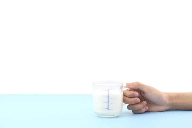 Concepto del día mundial de la leche Sostenga a mano un vaso de leche de vaca rústica fresca y fría rica en proteínas y calcio en una mesa azul con fondo blanco para el desayuno en la mañana