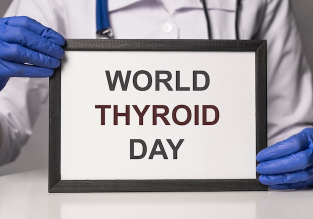 Concepto del día mundial de la tiroides. Inscripción sobre papel blanco en marco en manos del médico.