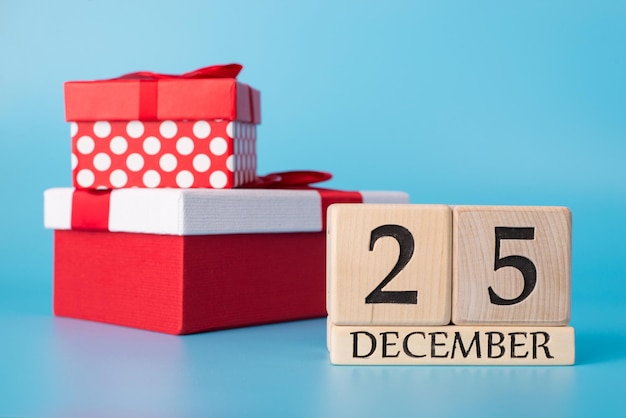 Concepto de día de Navidad. Foto de calendario de madera que muestra el 25 de diciembre y dos grandes cajas de regalo sobre fondo aislado sobre fondo azul con espacio en blanco vacío