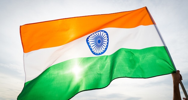 Concepto del día de la república india. Mano sosteniendo la bandera india sobre fondo de cielo.