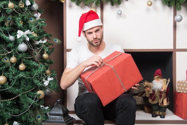 Concepto del día de San Esteban. Hombre con caja actual en el árbol de Navidad. Macho con sombrero de santa mantenga el paquete envuelto en la chimenea. regalo de navidad y año nuevo. Preparación y celebración de las vacaciones de invierno.