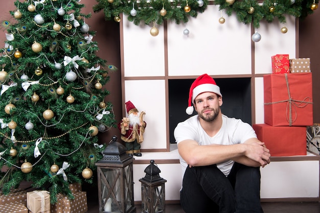 Concepto del día de San Esteban. Macho en el árbol de Navidad con cajas presentes. Preparación y celebración de las vacaciones de invierno. interior de la habitación de navidad y año nuevo. El hombre con sombrero de santa se sienta en la chimenea.