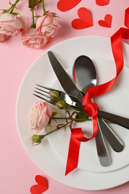 Concepto del día de San Valentín con cubiertos, rosas y cinta sobre fondo rosa