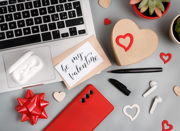 Concepto de día de San Valentín con gadgets modernos y vista superior de la tarjeta BE MY VALENTINE en mesa gris