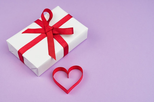 Concepto de día de San Valentín o cumpleaños con espacio de copia Corazón de cinta roja y caja de regalo en papel púrpura