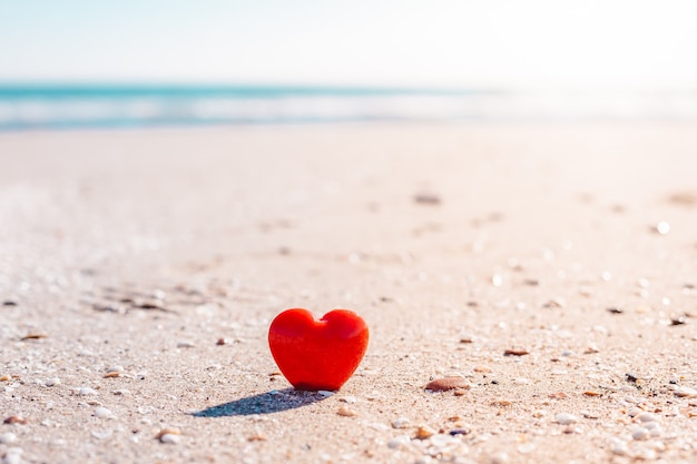 Concepto de día de San Valentín. Símbolo de amor romántico de corazón rojo en la playa de arena con espacio de copia.