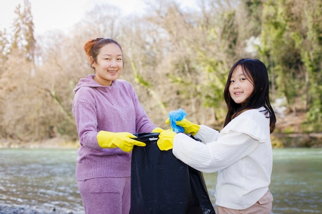 Concepto del Día de la Tierra Mujer e hija recogen basura en bolsas de basura limpiezas en la naturaleza para reciclar en sus comunidades limpian el río y protegen el medio ambiente de la conservación de la contaminación Naturaleza