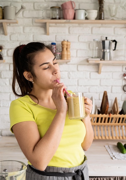 Concepto de dieta de alimentación saludable Mujer morena joven bebiendo batido de plátano de frutas en la cocina de casa de tarro de albañil