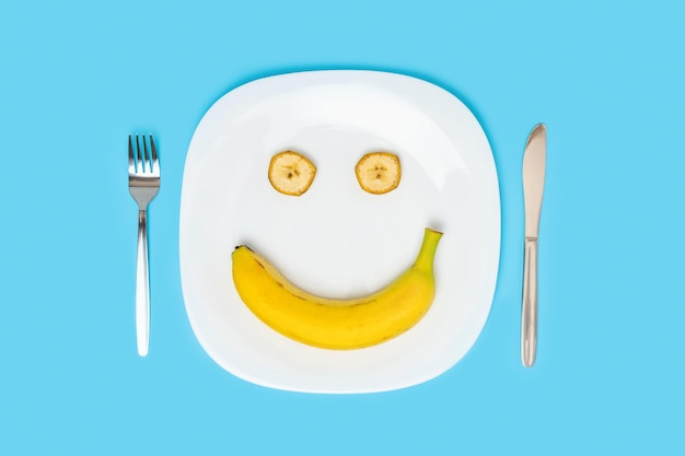 El concepto de dieta y alimentación saludable Sonrisa de plátano en un plato blanco sobre un fondo azul