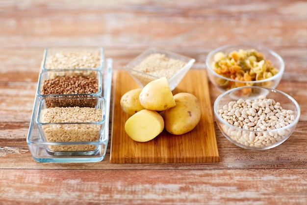 concepto de dieta, cocina, comida culinaria y carbohidrato - cierre de granos, pasta y frijoles en tazones de vidrio con papas en la mesa