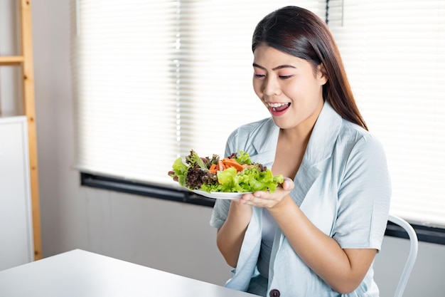 Concepto de dieta comiendo ensalada saludable. Mujer joven que sostiene el plato de verduras para una dieta saludable con una sonrisa en el cuidado de la salud.