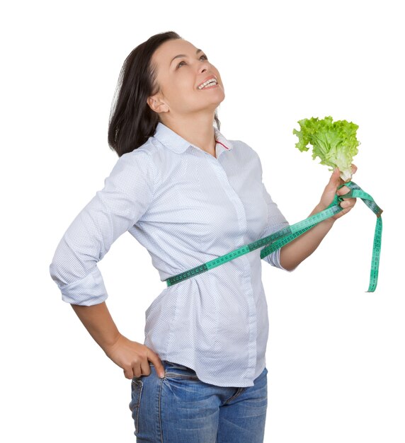 Concepto de dieta. Mujer joven con lechuga midiendo su cintura con cinta métrica sobre un fondo blanco.