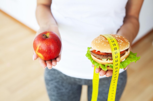 Concepto de dieta, mujer con una opción de hamburguesa dañina y manzana fresca.