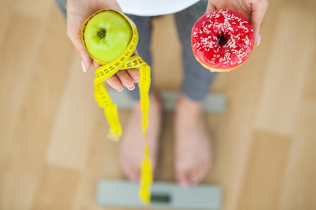 Concepto de dieta, mujer sosteniendo una opción de donut dañino y manzana fresca.