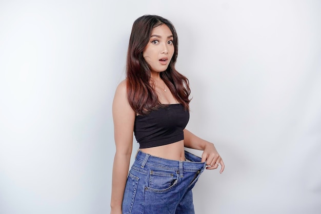 Concepto de dieta y pérdida de peso Una joven asiática en jeans de gran tamaño aislada en un fondo blanco