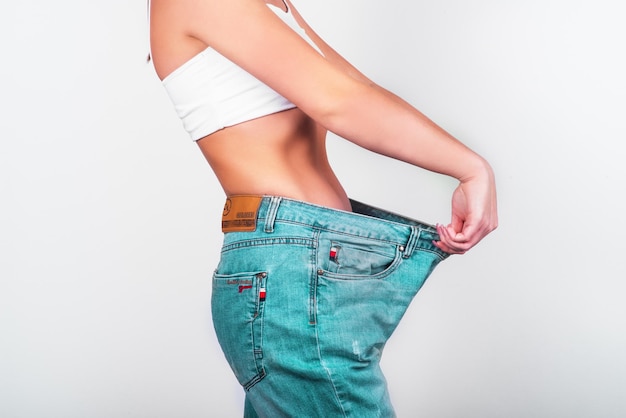 Concepto de dieta y pérdida de peso Mujer en jeans de gran tamaño sobre fondo blanco Cuidado del cuerpo