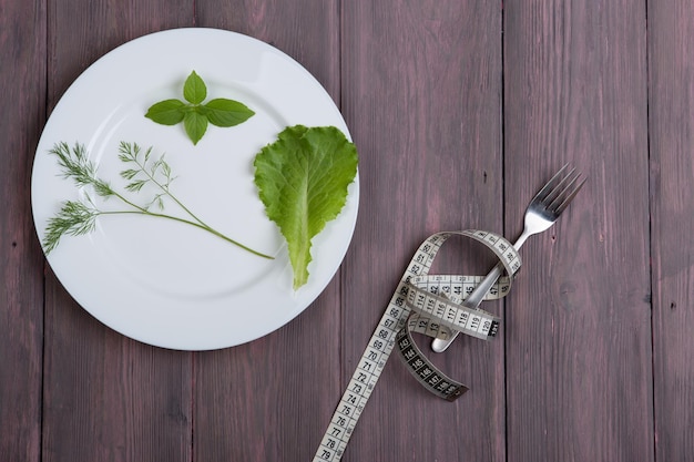 Concepto de dieta plato blanco con ensalada de eneldo lechuga tenedor de albahaca y cinta centimétrica