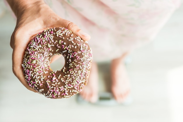 Concepto de dieta. Primer plano de los pies de la mujer en balanza con Donut. Concepto de dulces, comida chatarra poco saludable y obesidad.