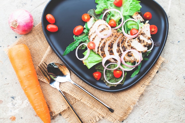 Concepto de dieta y salud. Ensalada de pollo a la parrilla servida en plato negro y mesa de concreto