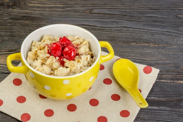 Foto el concepto de una dieta saludable. desayuno con mermelada de avena y frambuesas en un recipiente amarillo.