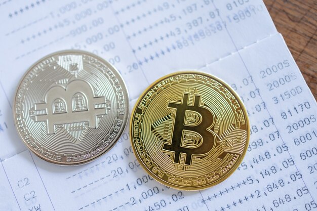 Concepto de dinero, finanzas y criptomonedas. Cerca de monedas Bitcoin de oro y plata en la libreta bancaria en la mesa de madera dorada.