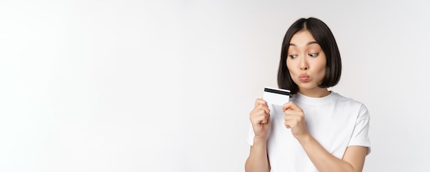 Concepto de dinero y finanzas linda chica japonesa besando su tarjeta de crédito de pie en camiseta sobre blanco b