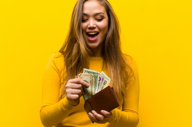 Concepto de dinero joven bonita mujer contra la pared naranja