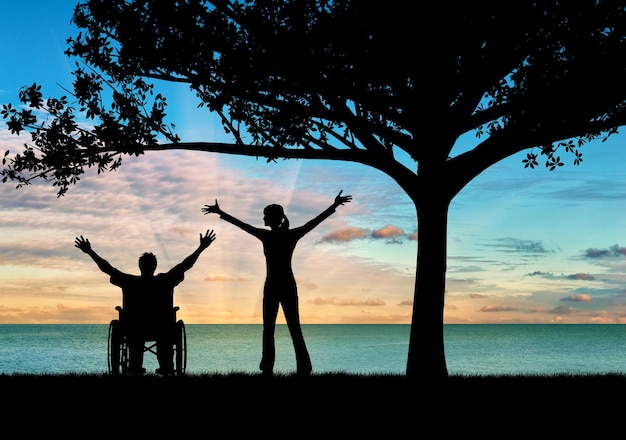 Concepto de discapacidad y enfermedad. Silueta feliz discapacitado y tutor bajo un árbol al atardecer