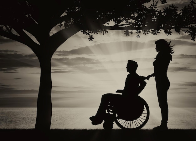Concepto de discapacidad y enfermedad. Silueta de persona discapacitada con un tutor en el mar al atardecer bajo las ramas de un árbol