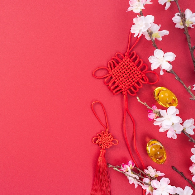 Concepto de diseño del año nuevo lunar chino - Hermoso nudo chino con flor de ciruelo aislado sobre fondo rojo, endecha plana, vista superior, diseño de arriba.