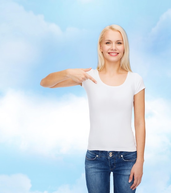 concepto de diseño de camisetas - mujer joven sonriente señalando con el dedo una camiseta blanca en blanco