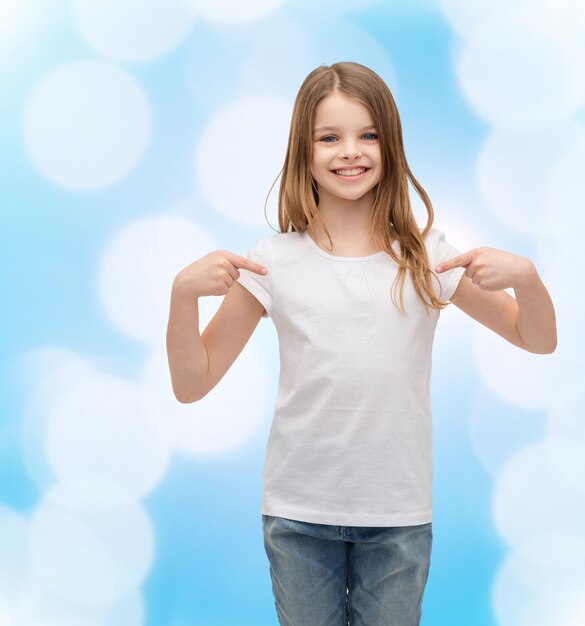 concepto de diseño de camisetas - niña sonriente con una camiseta blanca en blanco apuntándose a sí misma