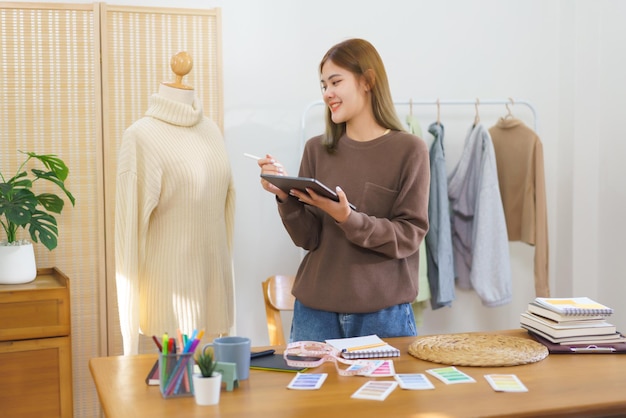 Concepto de diseño de moda Diseñador de moda sosteniendo una tableta para revisar el suéter antes de enviar al cliente