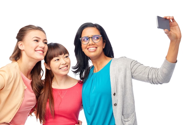 Foto concepto de diversidad, raza, etnia y personas: grupo internacional de mujeres felices y sonrientes sobre blanco tomándose selfie con un teléfono inteligente