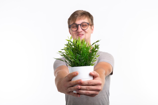 Foto concepto de diversión, broma, nerd y friki - hombre divertido que sostiene una flor en una maceta sobre una superficie blanca.