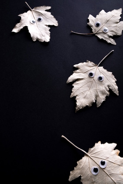 Concepto divertido de Halloween. Hoja de otoño con ojos como un fantasma sobre fondo negro. Vista superior, endecha plana