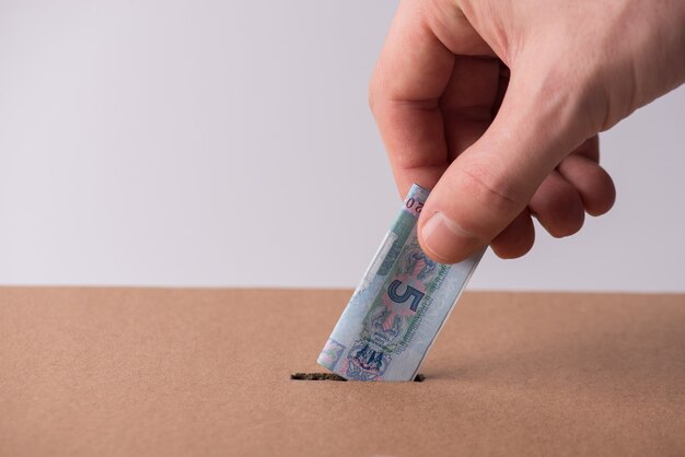 Concepto de donación de dinero. Foto de primer plano recortada de mano masculina poniendo dinero ucraniano doblado en una caja de cartón