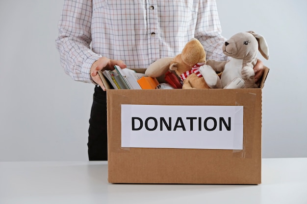 Concepto de donación. Hombre que sostiene la caja llena de libros y juguetes. Done para niños por favor